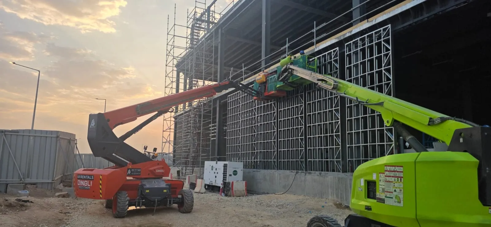 Boom lifts installing light-gauge steel framing on a data center in Riyadh at sunset